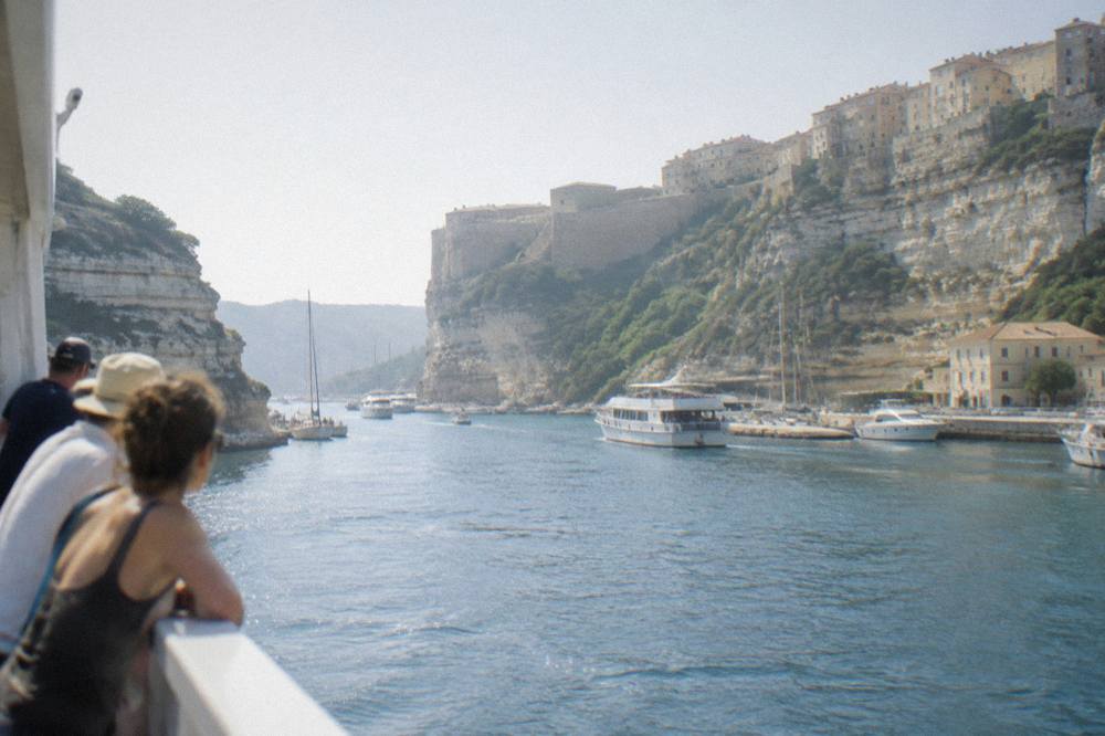 Passengers leaning on a ferry rail as the Corsican coastline passes by