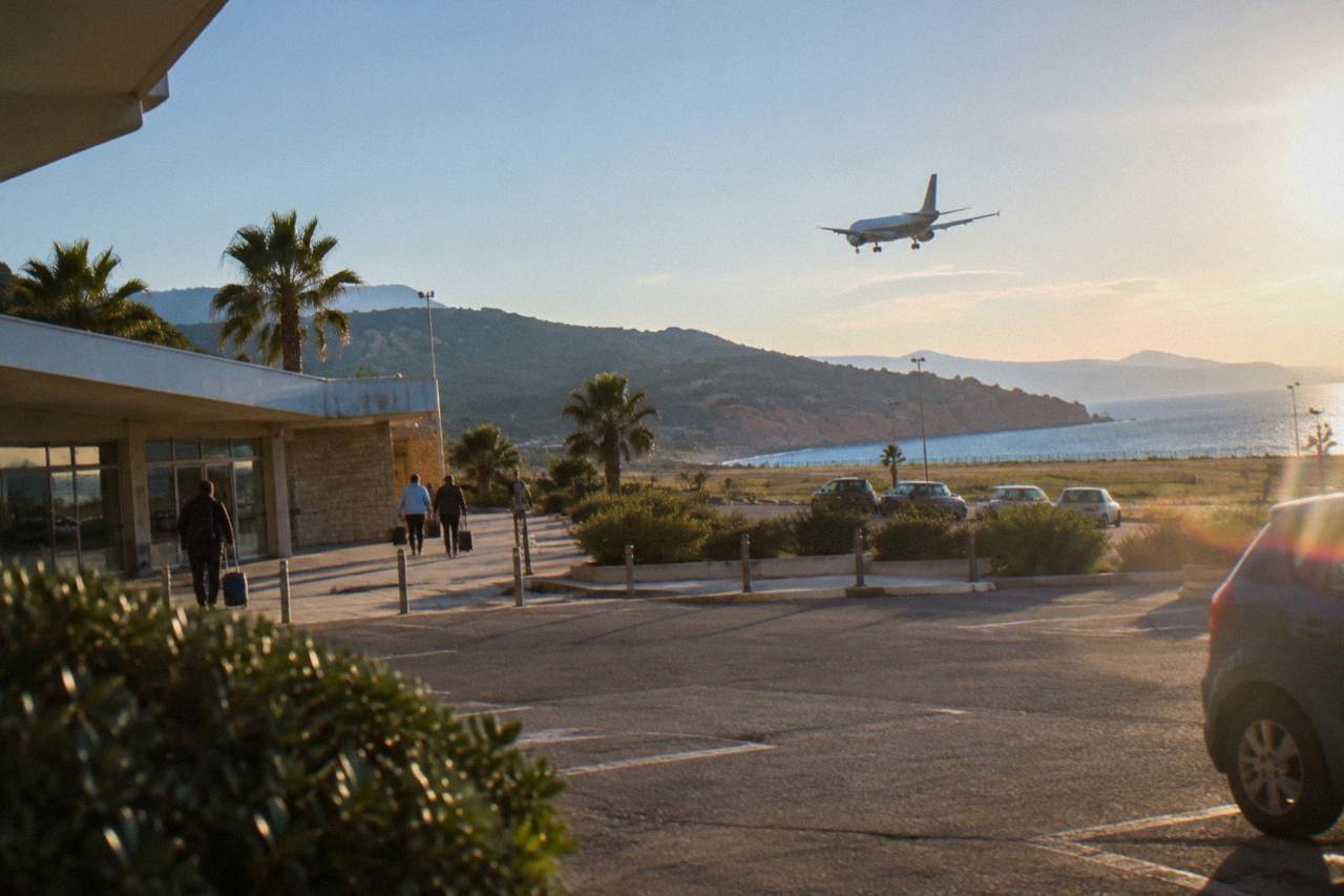 A plane descending over a Mediterranean coastline with red granite cliffs and turquoise water
