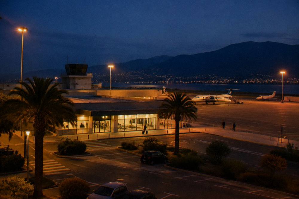An airport apron at dusk with small aircraft parked in front of Mediterranean hills