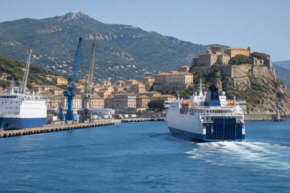 A ferry leaving a Corsican harbour with citadel walls above the water