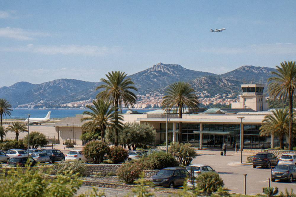A historic Mediterranean town square with ochre facades and a plane overhead at altitude
