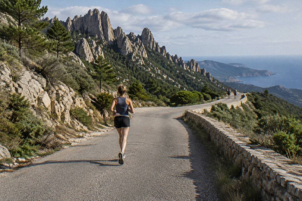 A narrow Corsican mountain road winding through rock and low scrub with sea in the distance