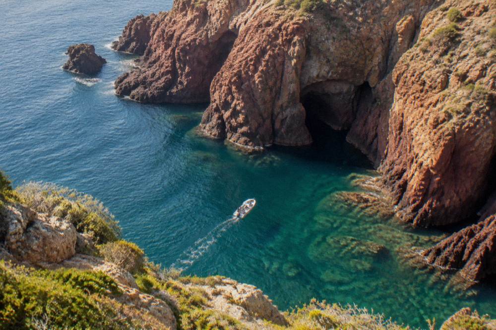 A small boat approaching red granite cliffs above clear water on the Corsican west coast