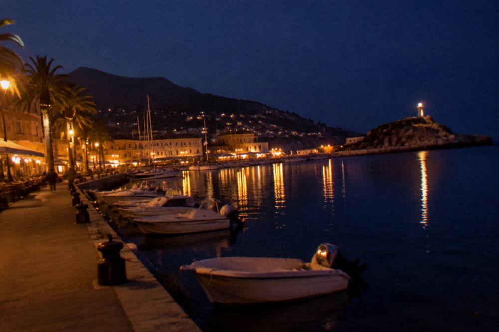 A harbour town at dusk with boats moored along the quay and hills behind