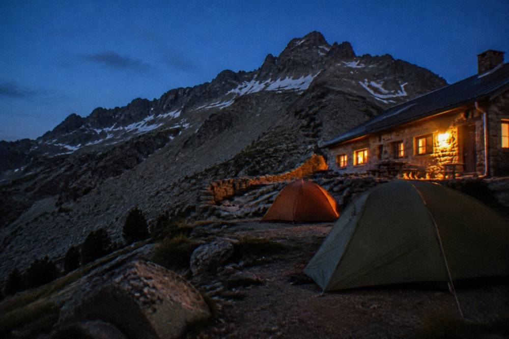 Tents pitched on a marked bivouac area beside a mountain refuge at dusk