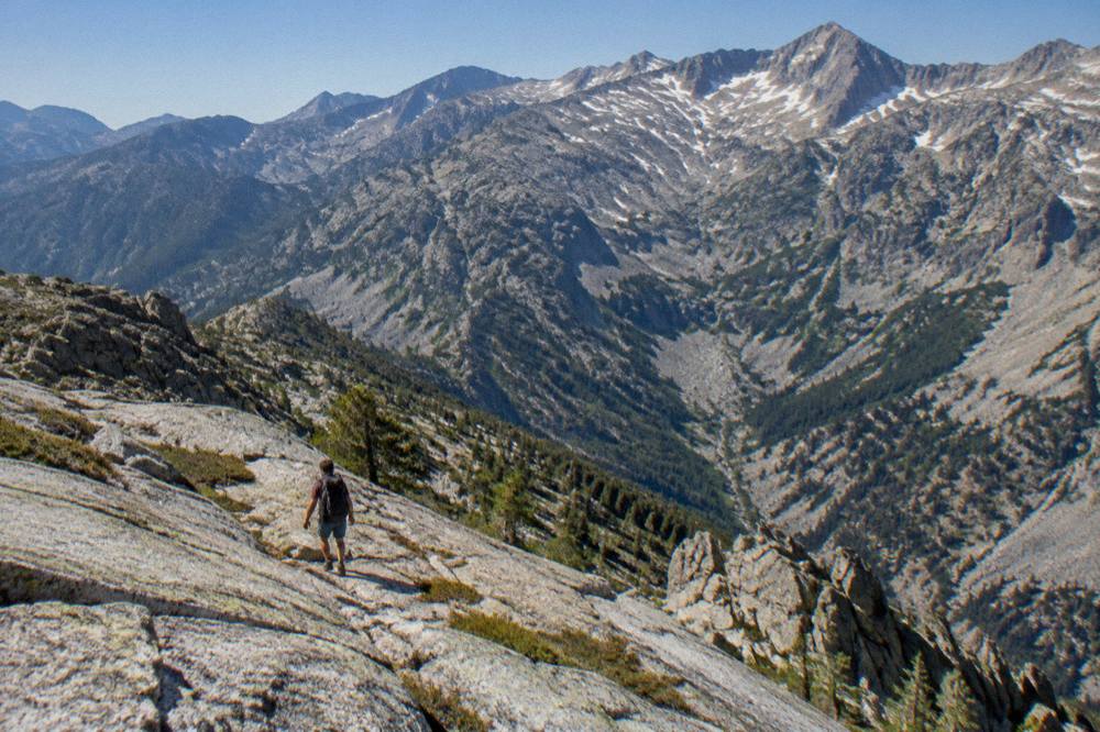 A hiker with a backpack crossing a granite slope above a deep valley