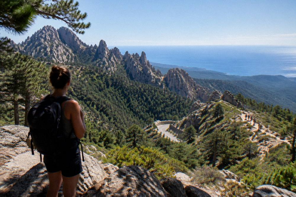 A hiker looking out over forested ridges toward the Mediterranean sea