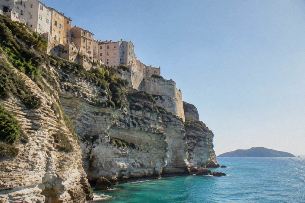 White limestone cliffs above a turquoise strait with a distant island on the horizon