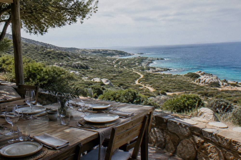 A set dining table on a shaded terrace overlooking the sea