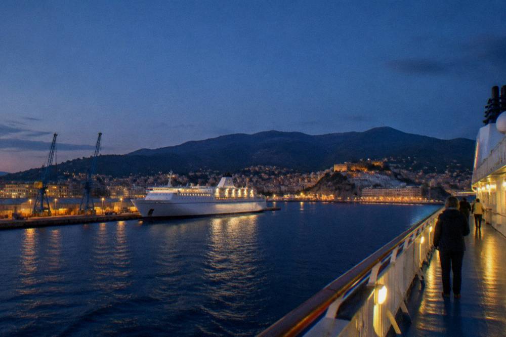 A ferry deck at night with the lights of the coastline receding behind