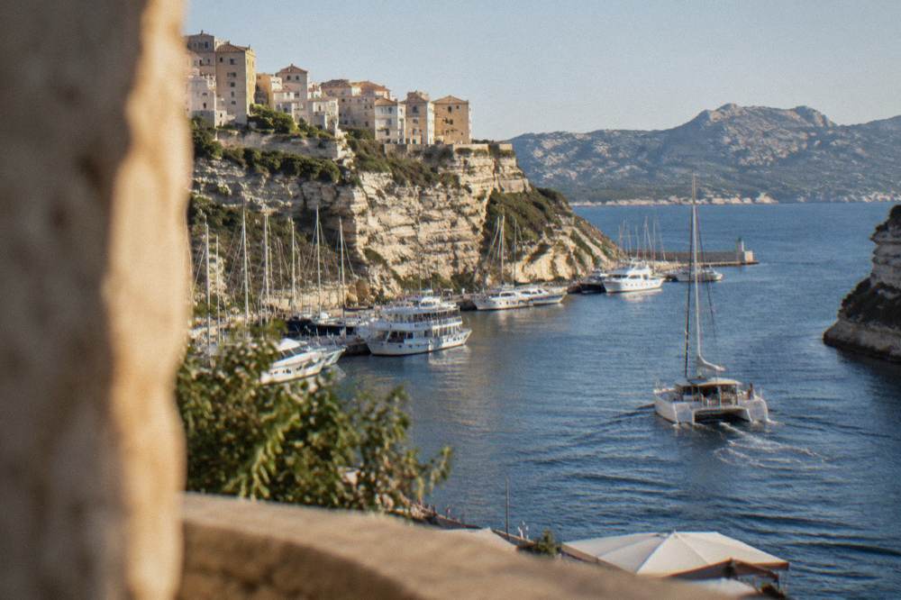 A catamaran underway on open water with a mountainous island coastline in the distance