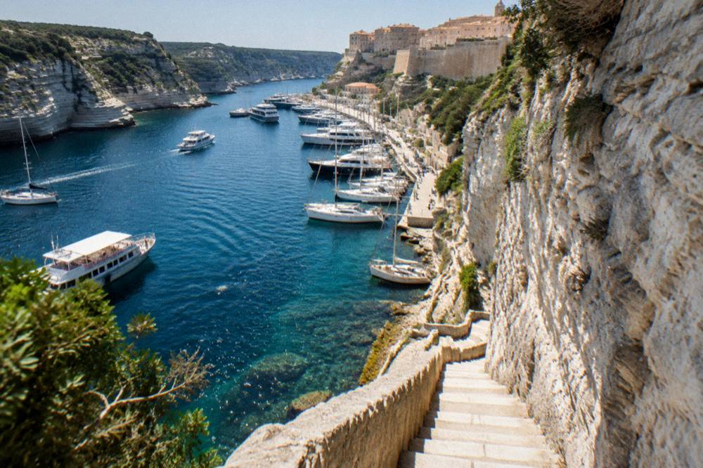 Stone steps cut into a tall cliff face descending toward clear water