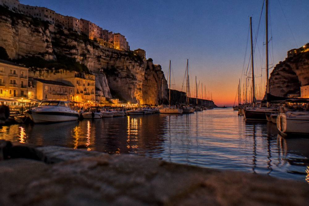 A harbour at dusk with masts of moored sailing boats against an orange sky