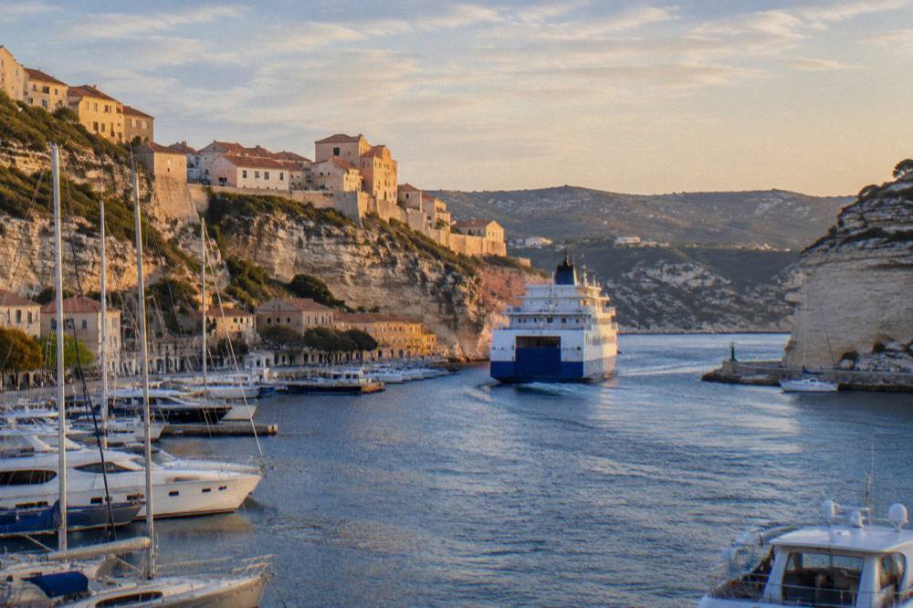 A ferry entering a harbour town with hills behind at golden hour