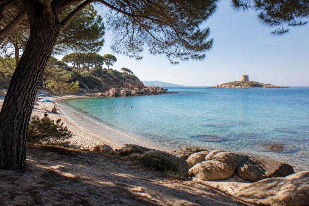 Granite rocks and calm turquoise shallows at the foot of a red cliff