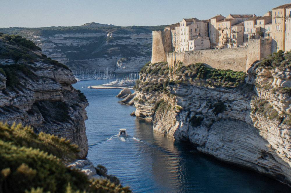 A small boat entering a narrow inlet between tall granite cliffs in Corsica