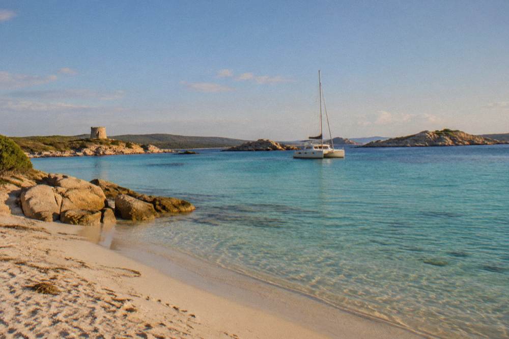 A catamaran anchored in clear shallow water near small granite islands
