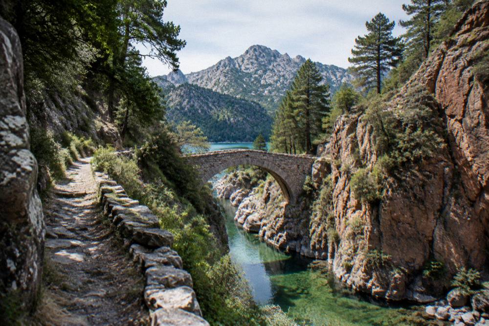 A turquoise mountain lake surrounded by pine trees and granite peaks in a Corsican gorge