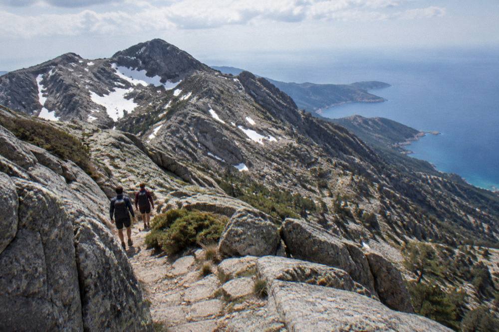 A couple walking a narrow stone path between granite rocks above the sea