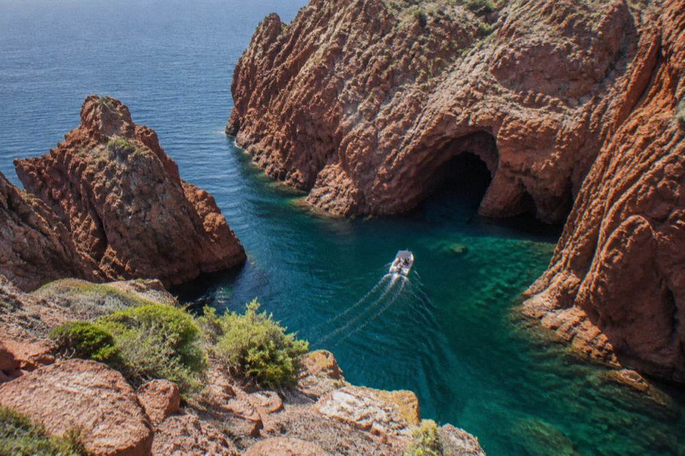 A small boat entering the red rock coves of the Scandola Nature Reserve on a clear day