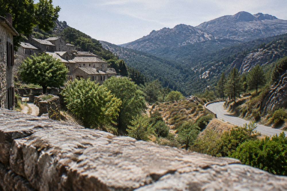 An empty winding mountain road through Corsican maquis under a summer sky