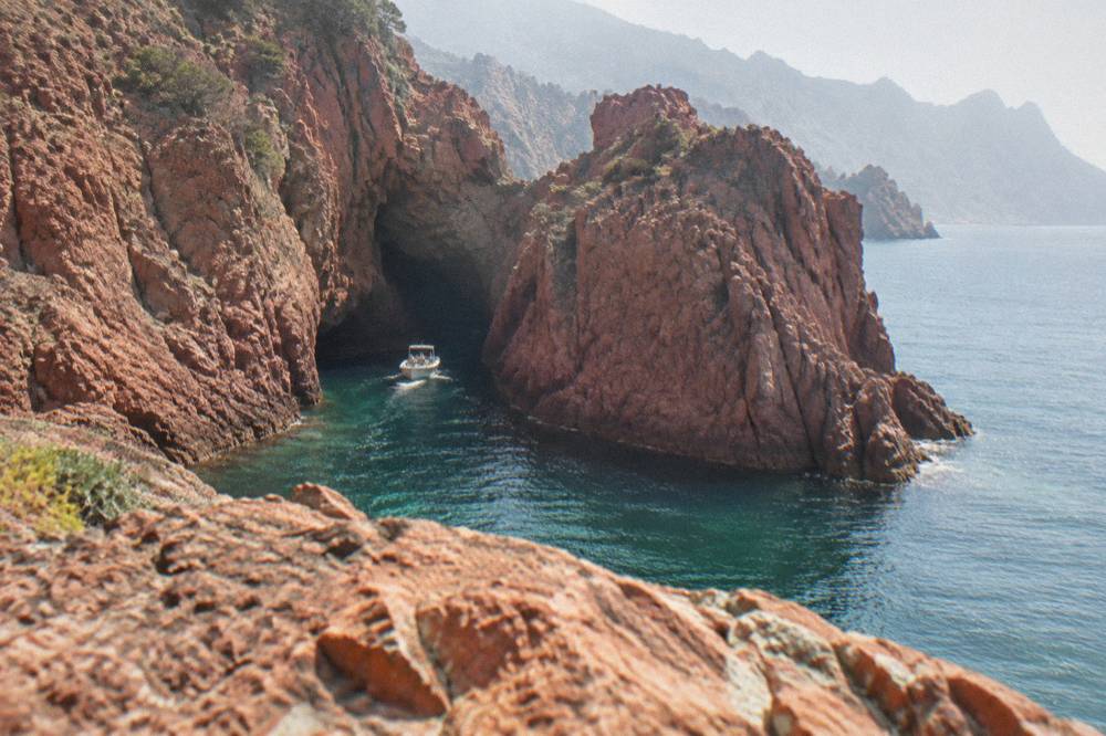 A small boat entering a red rock inlet in the Scandola reserve