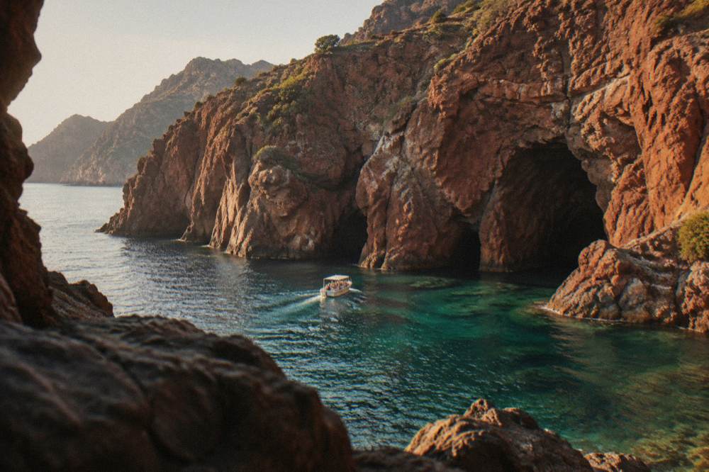 A small boat entering the red cliffs of Scandola nature reserve on clear water