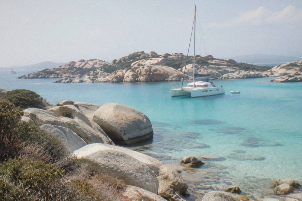 A catamaran moored in turquoise shallows among granite rocks at the Lavezzi islands