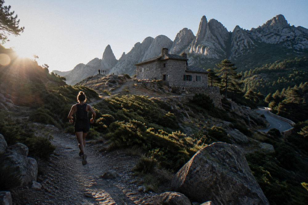 A stone refuge building on a mountain trail with granite peaks behind it
