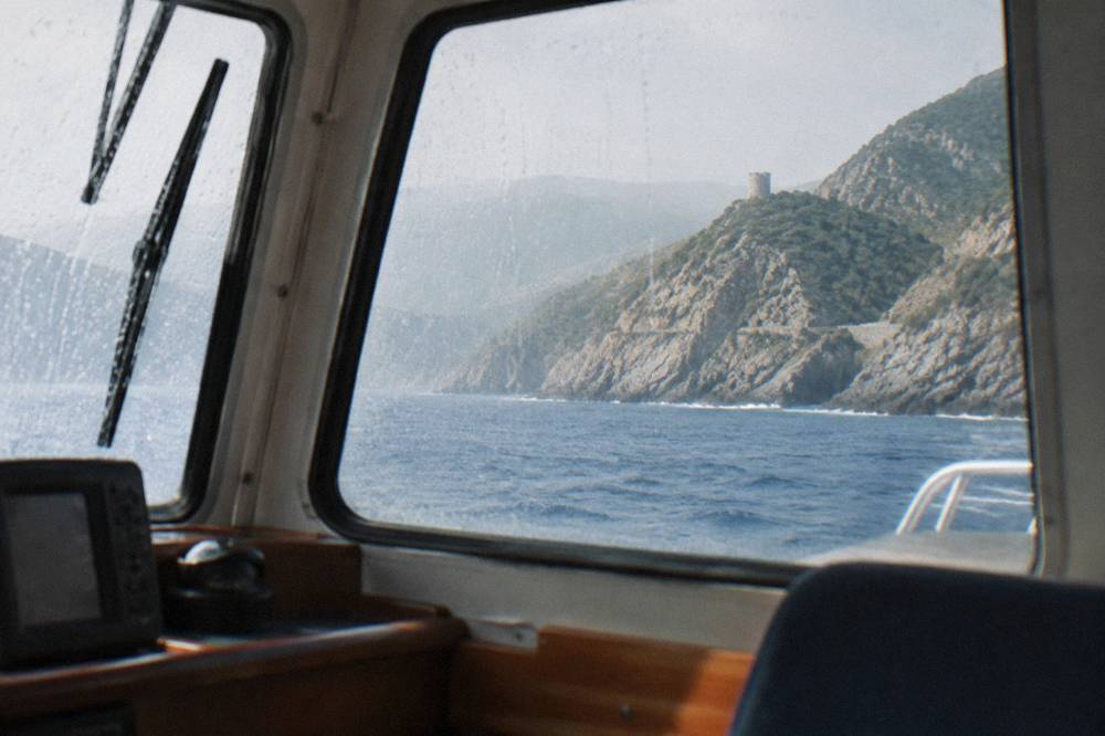 Boat cabin interior with rain-streaked windows and a view of dark cliffs beyond
