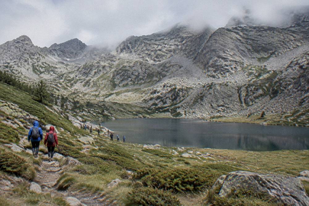 Hikers in rain jackets walking a mountain path with low cloud on the ridges