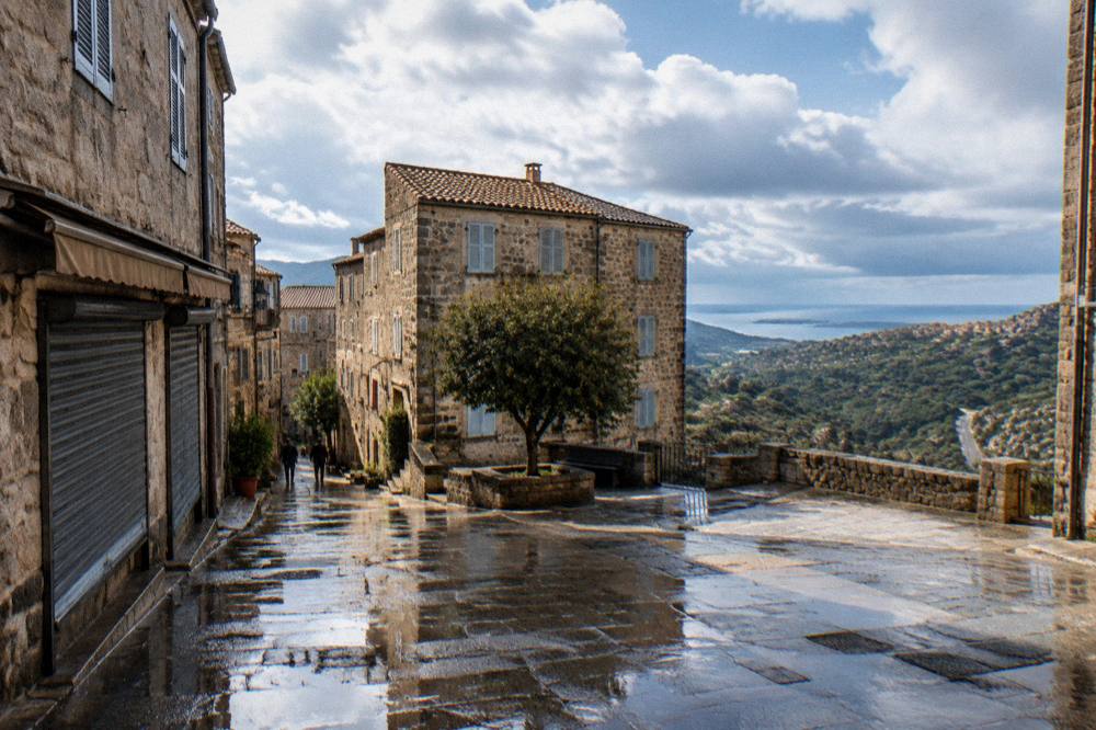 Wet street in a Corsican old town with reflections in the puddles and shuttered shop fronts