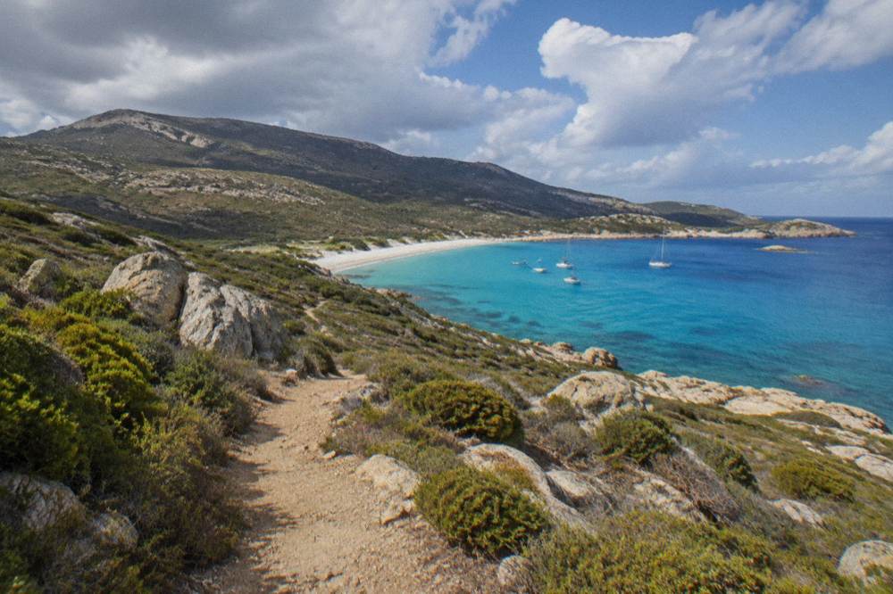 Boats anchored off a white sandy beach in the Désert des Agriates