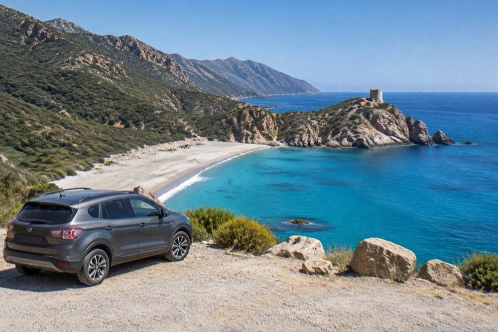 A parked car at a viewpoint above a Mediterranean bay in Corsica