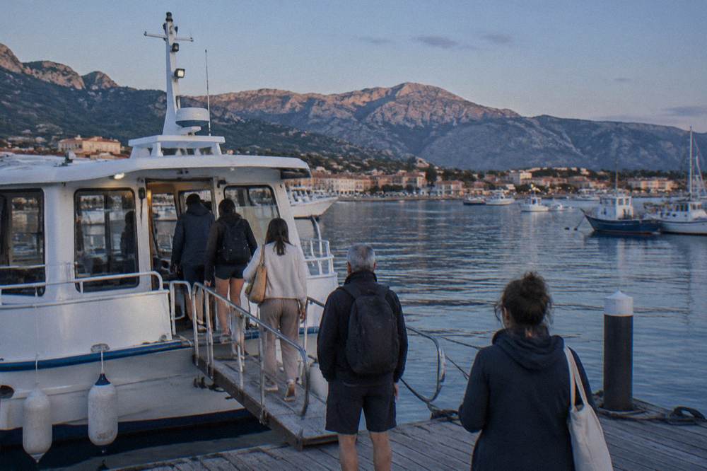 Passengers boarding a small white tour boat at a wooden pontoon in a Corsican harbour
