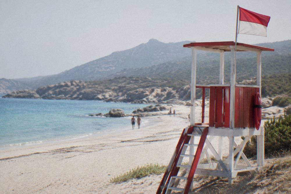 A red-and-white lifeguard post on a sandy Corsican beach with a flag flying