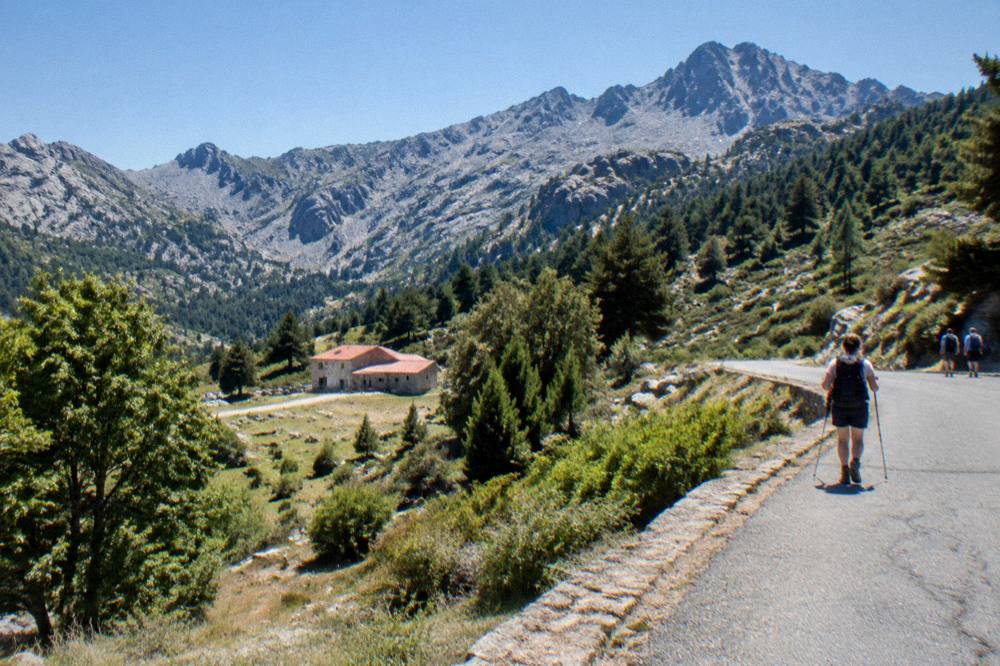 A stone refuge hut with a red roof below granite peaks at the end of a Corsican mountain stage