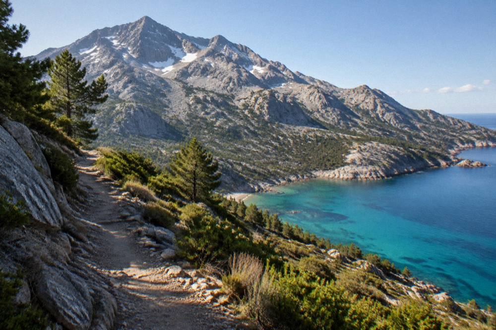An empty coastal path above turquoise water on the Corsican shore in early morning light