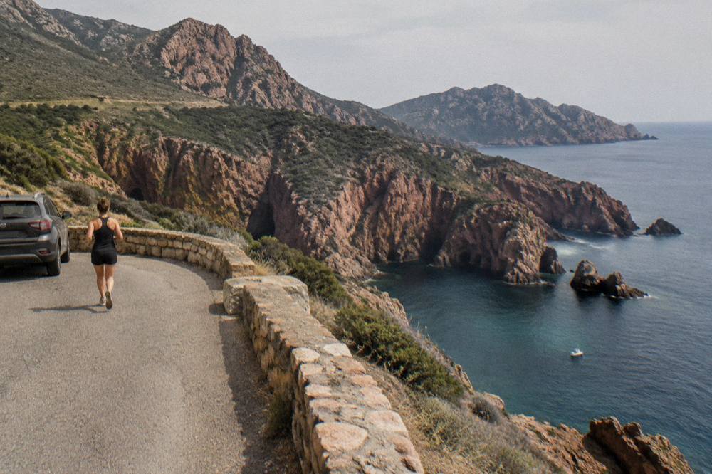 A car parked at a viewpoint above the sea on a winding coastal road in southern Corsica