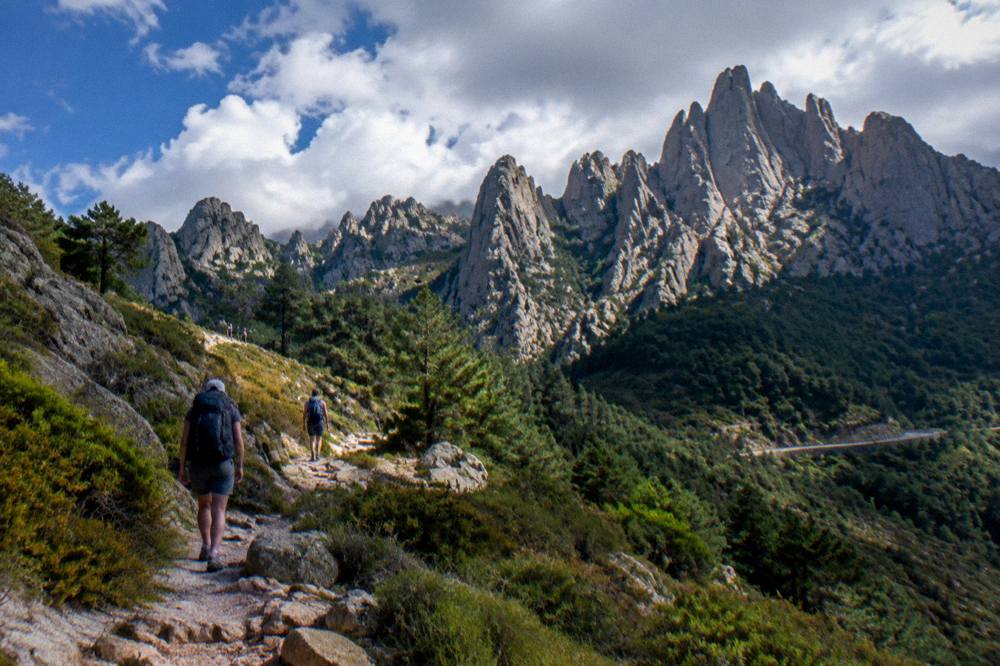 Hikers on a rocky mountain path below jagged granite peaks in central Corsica
