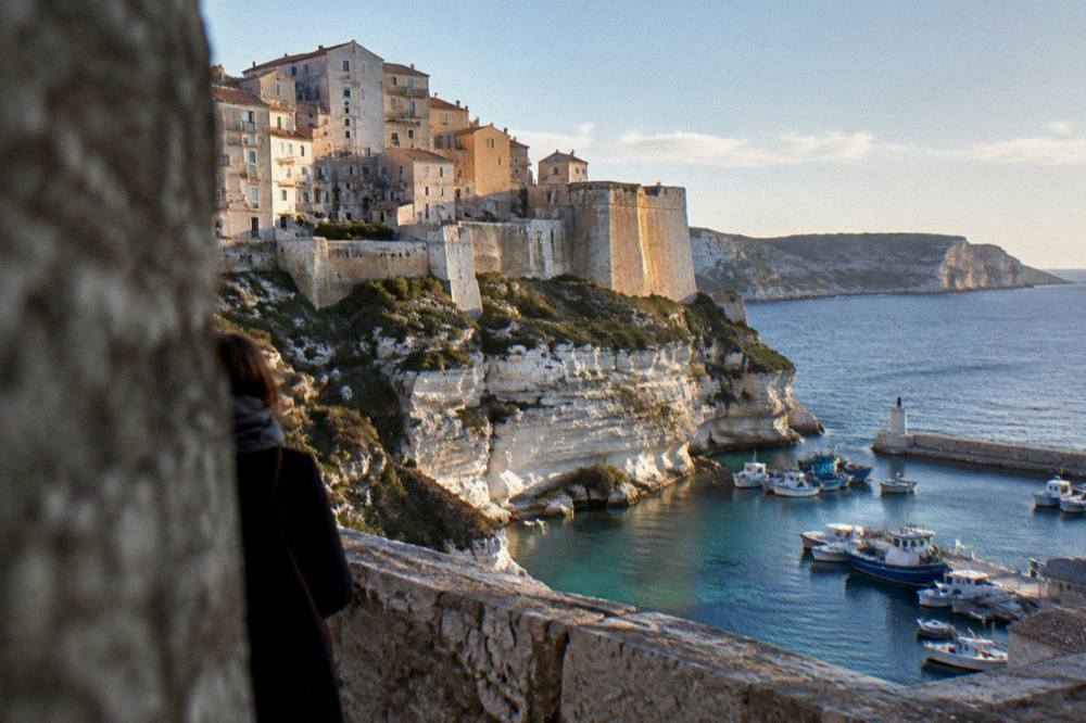 A stone citadel wall above a harbour with fishing boats in the evening light
