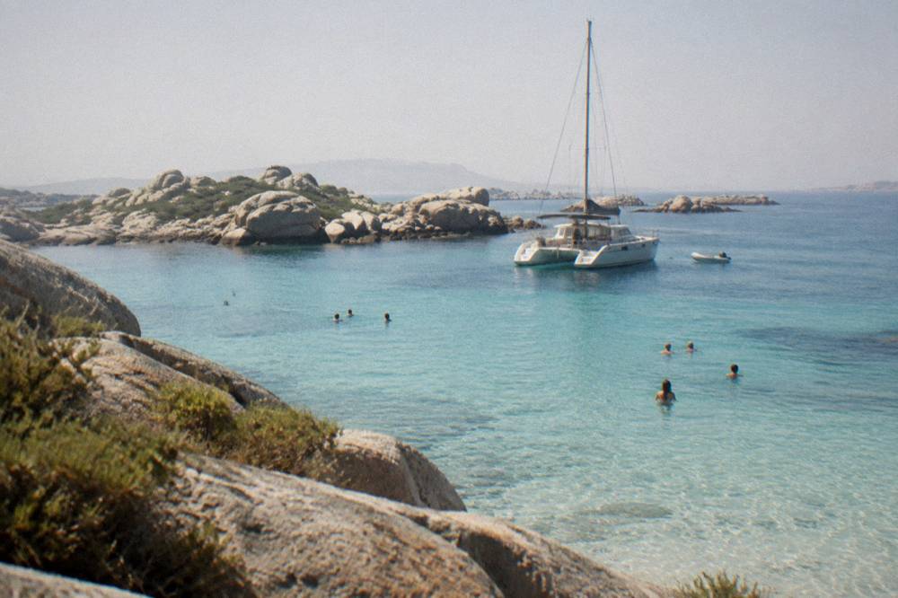 A catamaran anchored in a cove near the Lavezzi islands with swimmers in the water