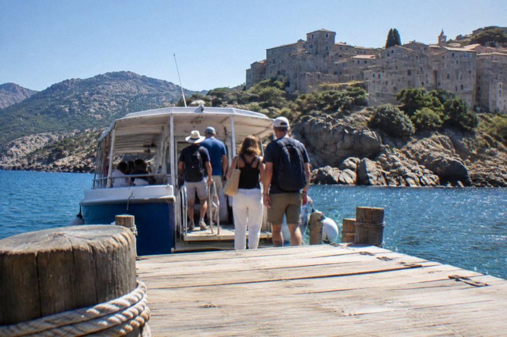 Passengers boarding a small tour boat at a wooden pontoon on the Corsican coast
