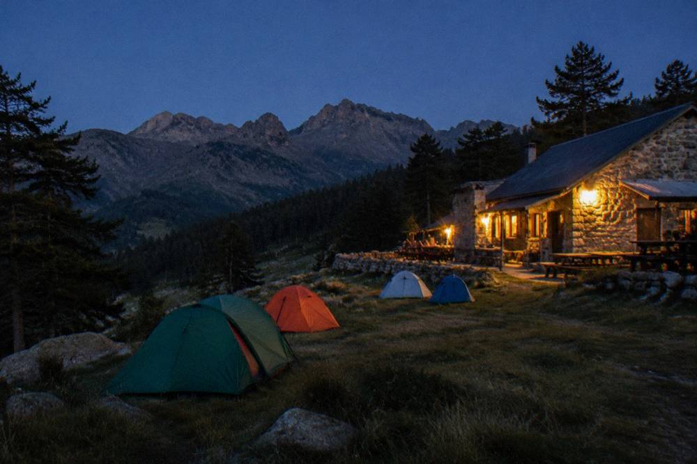 Colourful tents pitched beside a mountain refuge at dusk in the Corsican interior