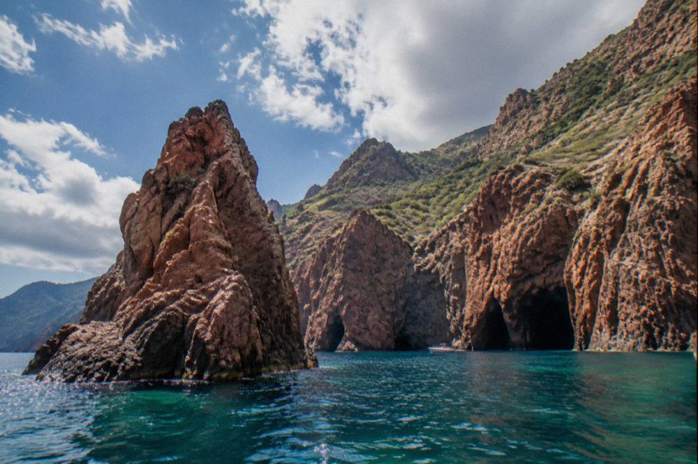 Red granite rock formations rising from turquoise sea at the Scandola Reserve