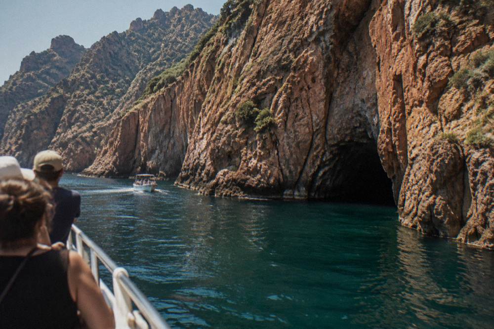 A tour boat passing close under tall cliffs with a cave opening at water level