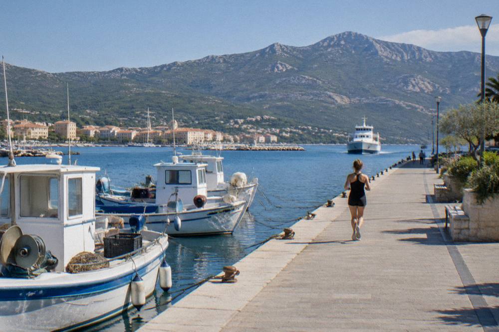 A ferry approaching a Corsican harbour town at dawn with hills behind